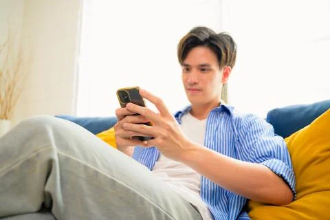 Portrait of young man using mobile phone and sitting on couch in living room Stock Photos