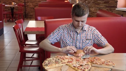 Portrait of a young man who eats a hamburger in a street food cafe. Fast food co Stock Footage 102718424