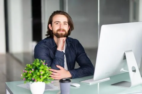 Portrait of young man working on computer sitting at his desk in the office Stock Photos