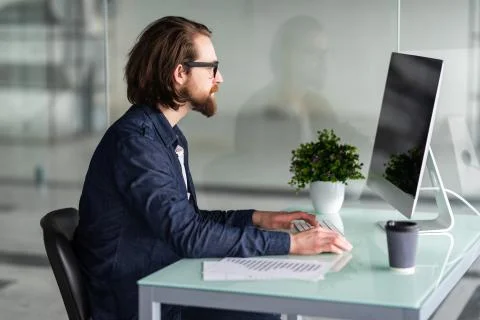 Portrait of young man working on computer sitting at his desk in the office Stock Photos