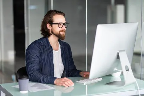 Portrait of young man working on computer sitting at his desk in the office Stock Photos