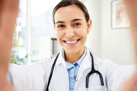 Portrait of a young mixed race female doctor taking a selfie while smiling and Stock Photos