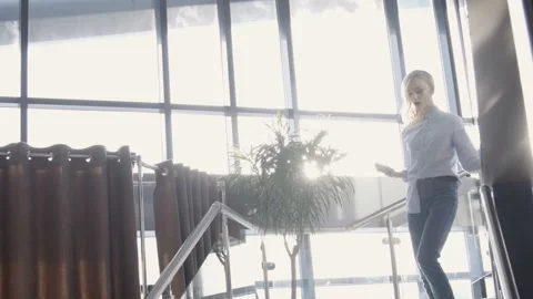 Portrait of young model is going downstairs in sunny hall with glass wall, slow Video stock 86461316