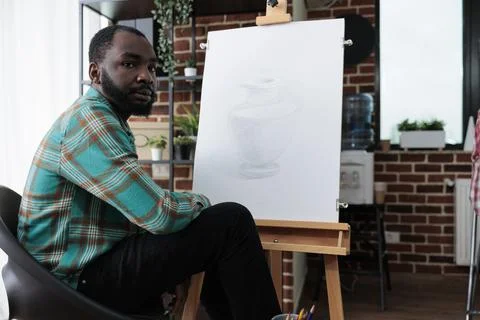 Portrait of young painter sitting in front of white canvas drawing sketch Foto stock