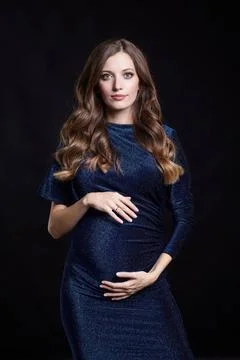 Portrait of young pretty pregnant woman on black studio background. Female... Stock Photos