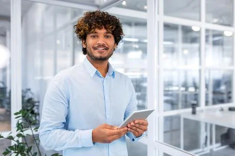 Portrait of young programmer with tablet computer inside office, hispanic man Stock Photos