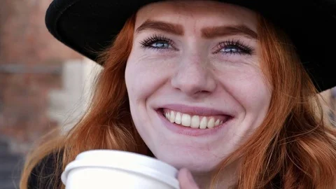 Portrait of young red haired lady with hat drinking coffee and smiling Stock Footage 78250018