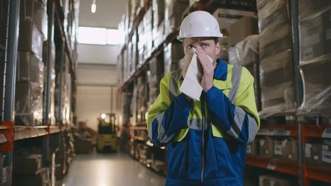 Portrait of young sick warehouse worker blowing his nose while standing in Stock Footage 123279329