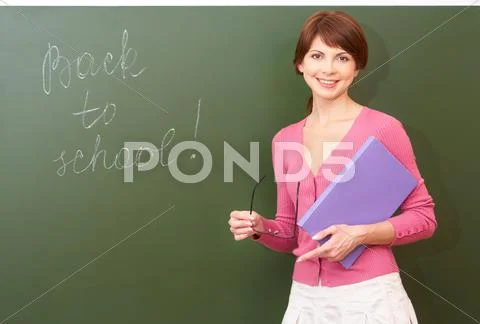 Portrait of young teacher with book and eyeglasses looking at camera by the blac Stock Photos