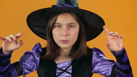 Portrait of Young Witch Casting Evil Spells on Halloween on Orange Backdrop Stock Footage 285001318