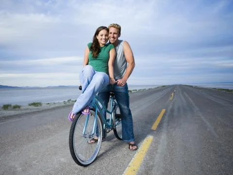 Portrait of a young woman and a mid adult man sitting on a bicycle Stock Photos