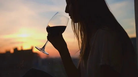 Portrait of young woman drinking red wine from a glass and watching on sunset Stock Footage 77375341