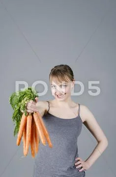 Portrait of young woman holding carrots against grey background Stock Photos
