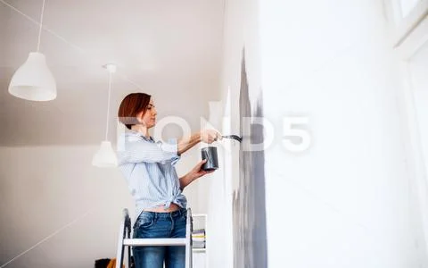 A portrait of young woman painting wall black. A startup of small business. Stock Photos