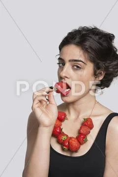 Portrait of a young woman wearing strawberry necklace as she eats one piece over Stock Photos