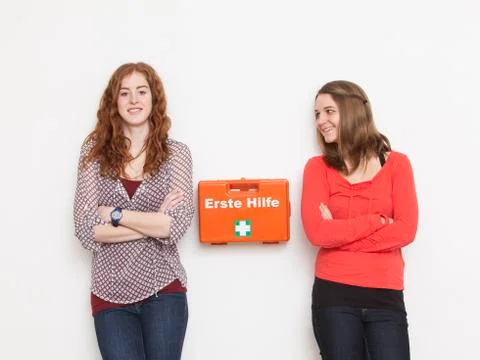 Portrait of young women leaning against wall with first aid kit, smiling Stock Photos