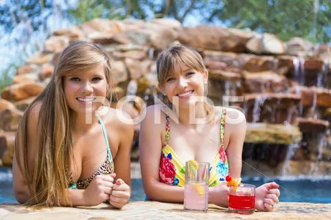 Portrait of young women sitting at swimming pool, smiling Stock Photos