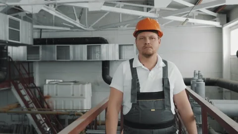 Portrait of a young worker in a uniform and hard hat, walking through a factory. Stock Footage 306816089
