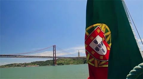 Portuguese flag on a ship on background of 25th April bridge and Jesus statue Stock Footage 64578281