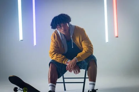 Posing man wearing bomber jacket leaning on folding chair in lighting studio, Stockfoto's
