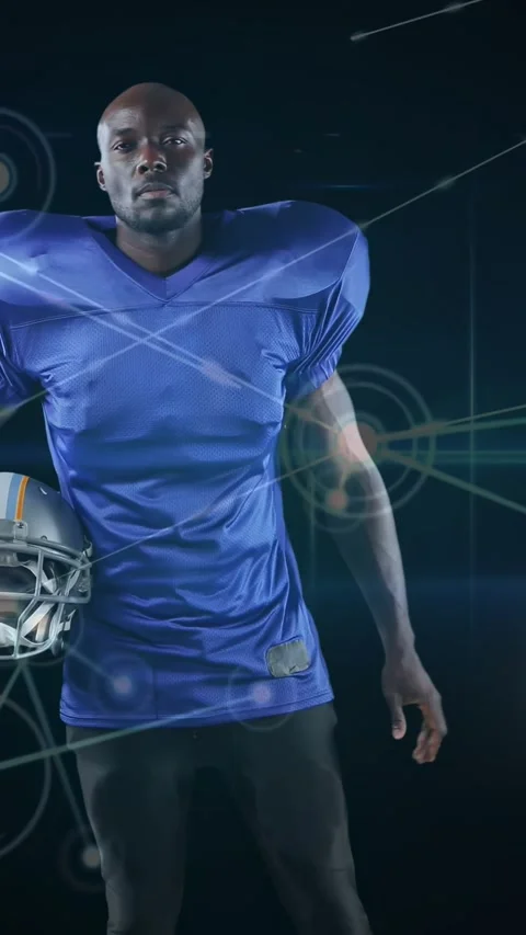 Posing player in blue jersey with shoulder pads in studio, holding silver helmet Stock Footage 331046945