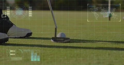 Positioning putter head behind golf ball on putting green beside golf shoe, w Stock Photos
