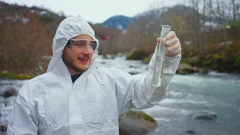 Positive and smiling ologist in a protective white jumpsuit tests the water Stock Footage 233976994