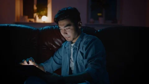 Positive Asian guy browsing the web sites on tablet home at night. Stock Footage 105585218