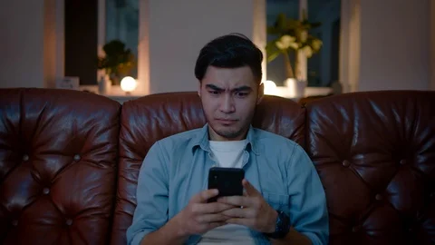 Positive Asian guy thinking about what to write up in chat on mobile phone. Stockbeeldmateriaal 105752892