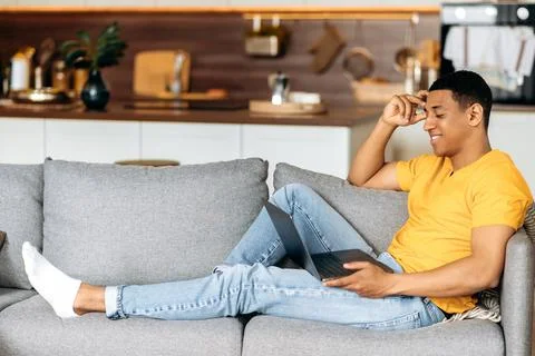 Positive attractive hispanic guy sitting on a sofa at home in the living room Stock Photos