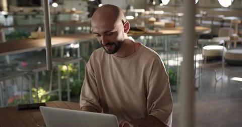 Positive bald guy sitting at cafe and typing on laptop Stock Footage 159082894