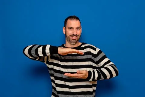 Positive bearded man in striped pullover holding something invisible in his h Stock Photos