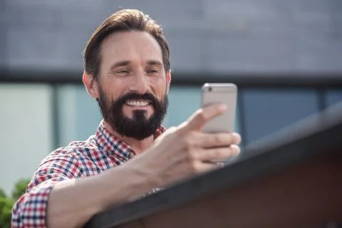 Positive bearded man using his phone outdoors Stock Photos