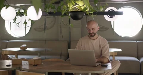 Positive bearded man working on laptop at cozy cafe Stock Footage 159083479