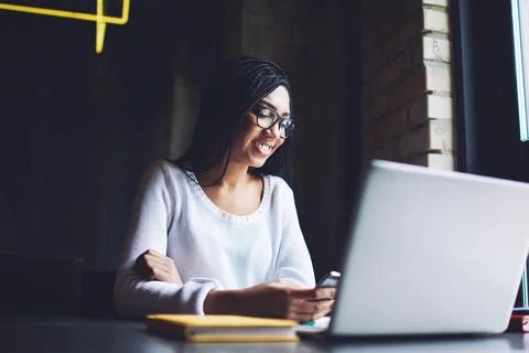 Positive black freelancer using smartphone while working on netbook in cafe Stock Photos
