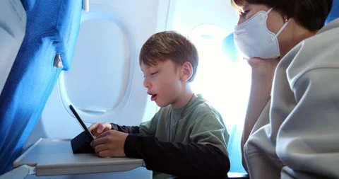 Positive boy engaged with education on tablet with during flight, mother watch Stock Footage 303993533