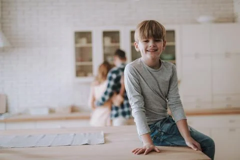 Positive boy sitting on the table in the kitchen and smiling Stock-Fotos