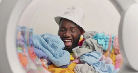 Positive dark skinned bearded man has sleepy expression fall asleep in laundry Stock Footage 157337339