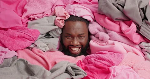 Positive dark skinned man arranges closet sticks head in pile of laundry. Happy Stock Footage 156969676