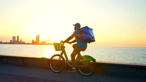 A positive deliveryman in a blue uniform with a backpack rides a bicycle Stock Footage 237446991