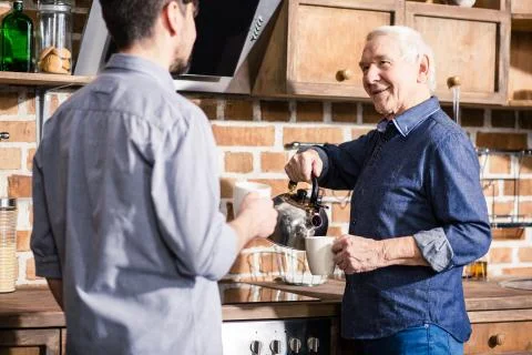 Positive elderly man drinking tea with his son Stock Photos