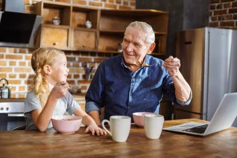 Positive elderly man having breakfast with his granddaughter Stock Photos