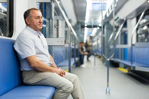 Positive elderly man sitting in an empty subway carriage while train is moving Stock Photos