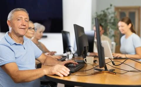 Positive elderly man using computer to surf internet in library Stockfoto's