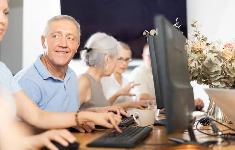 Positive elderly man using computer to surf internet in library Fotos de archivo
