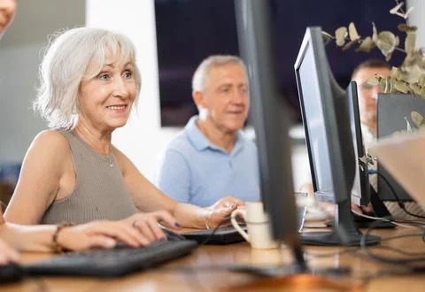 Positive elderly woman using computer to surf internet in library Fotos de archivo