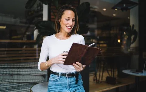 Positive female checking notes in notepad planning working day in cafe Stock Photos