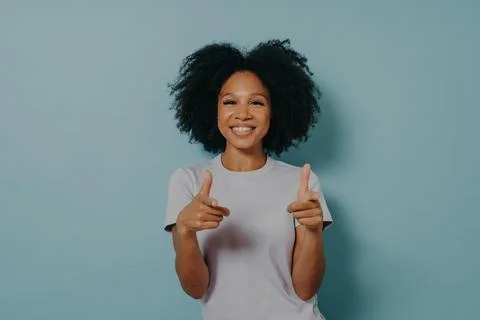 Positive friendly dark skinned lady making finger gun gesture while standing on Stock Photos