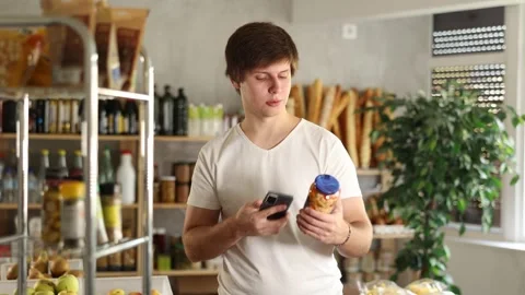 Positive guy purchaser scanning QR code or barcode of canned beans in 動画素材 341379120