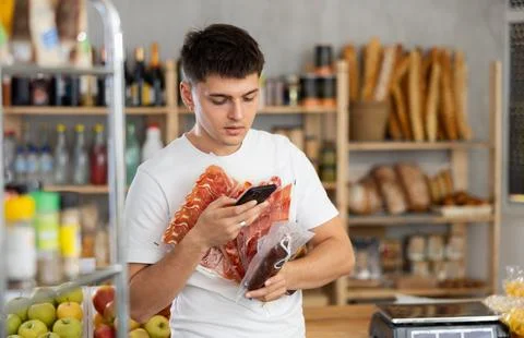Positive guy purchaser scanning with smartphone QR code of dried sausage or Foto stock
